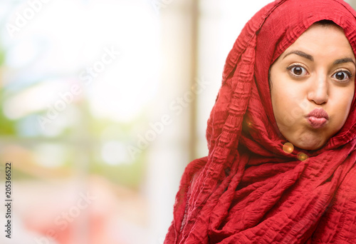 Young arab woman wearing hijab puffing out cheeks, having fun making funny face