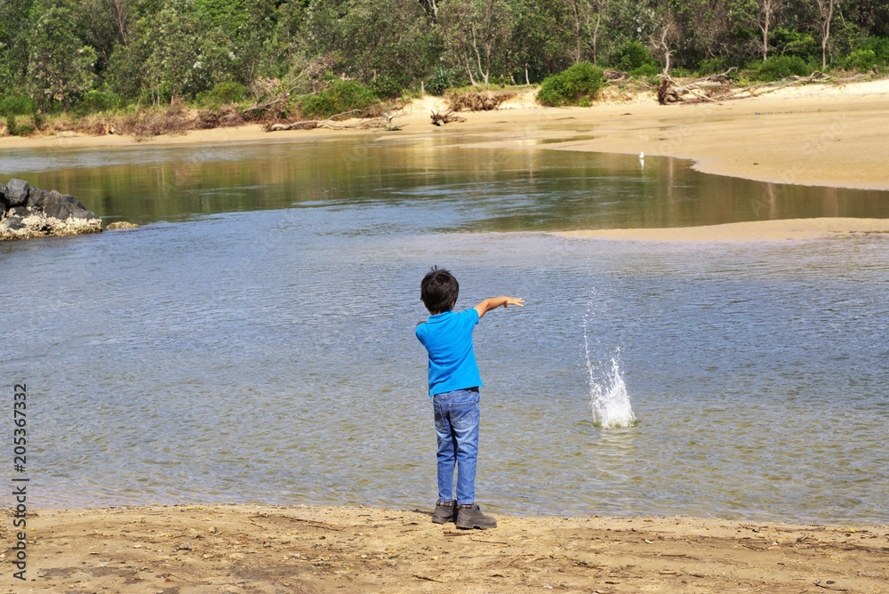 Kid throwing stone in water. Child in action of throwing stone or rock in water.