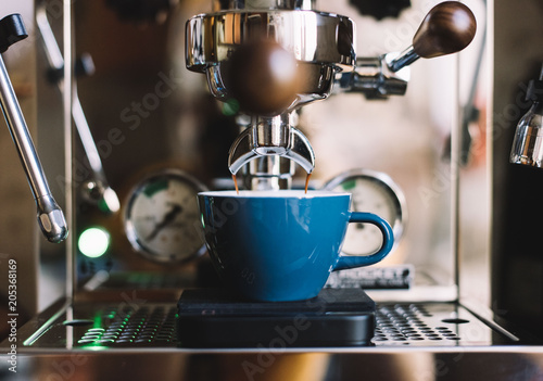 Wallpaper Mural Delicious fresh morning double espresso coffee with a beautiful crema in a blue ceramic cup with a saucer standing on a metal drip tray of an espresso machine, close up view Torontodigital.ca