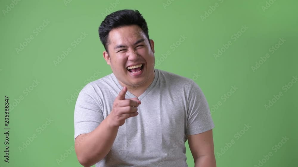 Young handsome overweight Asian man against green background