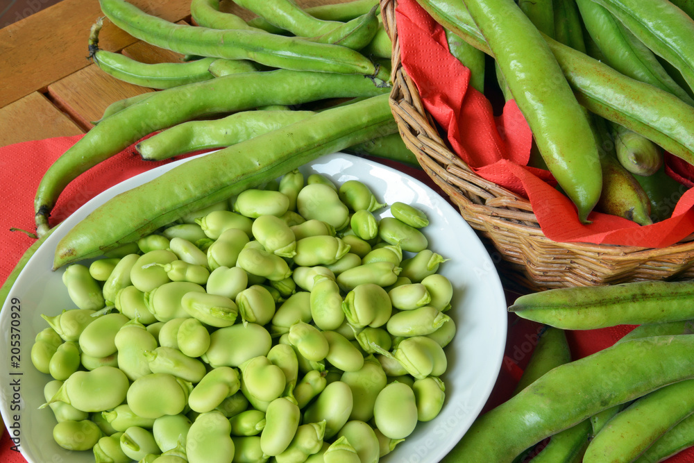 fave fresche ,sbucciate dentro ad un piatto, a fianco le fave con la buccia