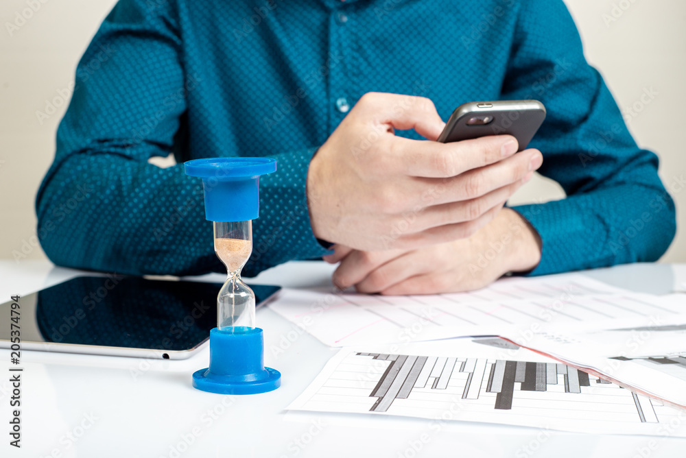 Hourglass. Businessman working in the office in the background. Concept time is money. Hourglass. Businessman working in the office in the background. Concept time is money.