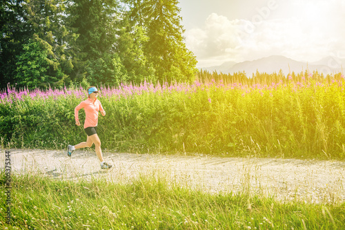 Woman trail running on country road in mountains, summer day
