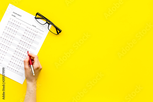 Take the exam, write the exam. Hand with pen near exam paper on yellow background top view copy space photo