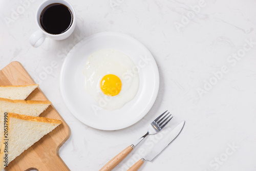 Top view of white dish with fried egg on white background.