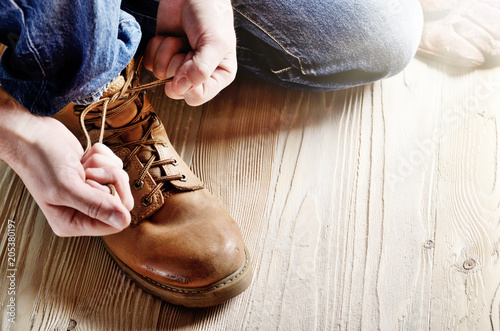 Obraz na płótnie Carpenter in blue jeans tying shoelaces of yellow work boots on on wooden floor. Place for text w salonie