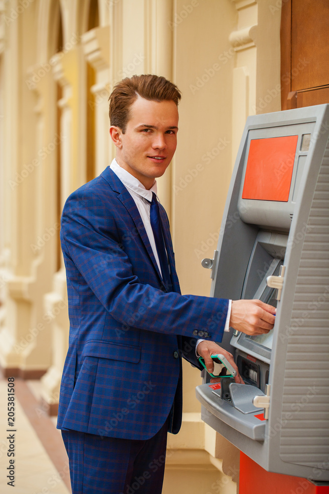 A young businessman stands near an ATM in a shopping center A young businessman stands near an ATM in a shopping center