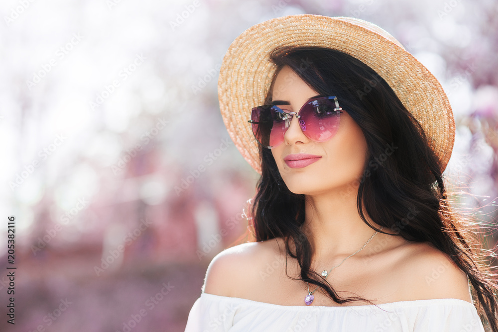 Outdoor close up portrait of young beautiful woman wearing stylish sunglasses, straw boater hat, white cold shoulder blouse. Spring, summer fashion concept. Copy, empty space for text