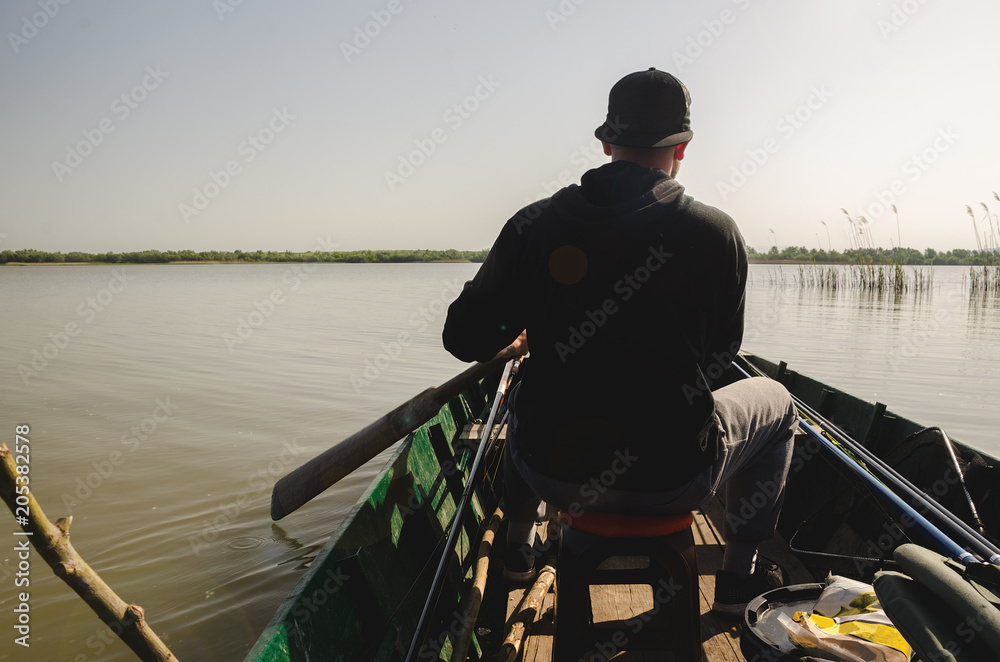 Young man rowing a boat while looking for place to fish Young man rowing a boat while looking for place to fish