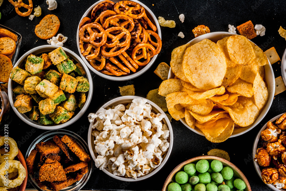 Variation different unhealthy snacks crackers, sweet salted popcorn, tortillas, nuts, straws, bretsels, back chalkboard copy space Variation different unhealthy snacks crackers, sweet salted popcorn, tortillas, nuts, straws, bretsels, back chalkboard copy space