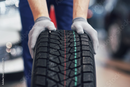 Closeup of mechanic hands pushing a black tire in the workshop