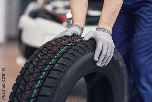 Closeup of mechanic hands pushing a black tire in the workshop