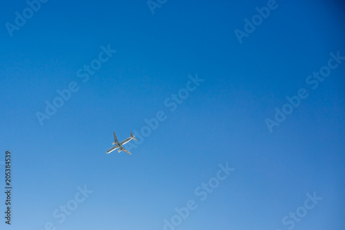Passenger airplane flies overhead on clear blue sky background with no clouds. Bottom view
