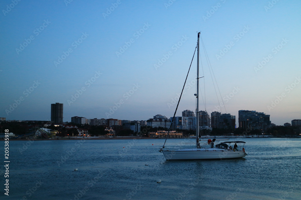 The image of a yacht sailing in the evening, against the backdrop of the city.