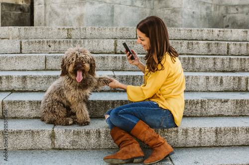 Young beautiful woman taking photograph of her sweet dog playfuly in a lovely park of the center of Madrid. Seated in stone stairs. Lifestyle photo