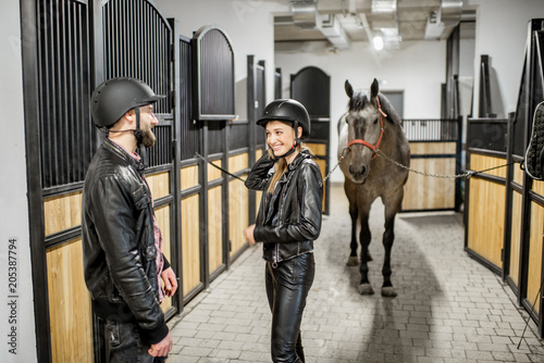 Young couple in leather jackets and protective helmet standing in the horse stable © rh2010