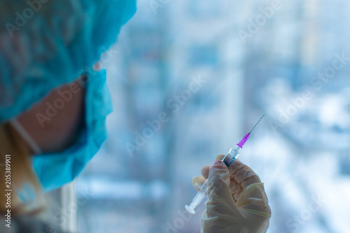 A nurse is holding a syringe with a vaccine on a light background.