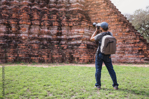 Young Asian traveling backpacker taking photos with camera in Bangkok, Thailand.Male traveler photographing temples at Bangkok.