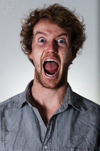 Young man screaming in stress on grey background