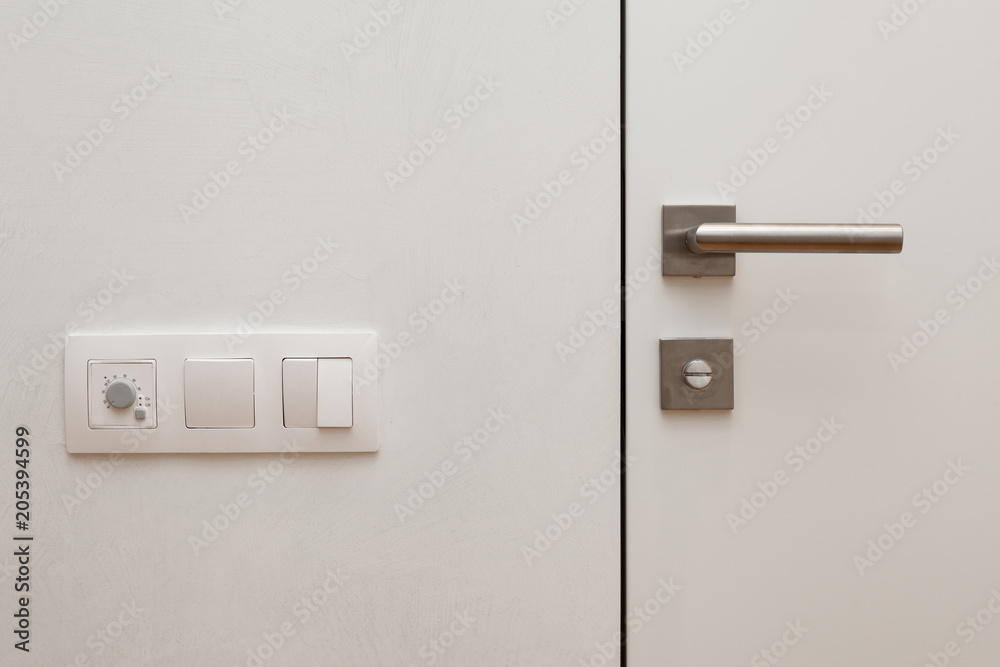 Light switch next to the white door with metallic handle Light switch next to the white door with metallic handle