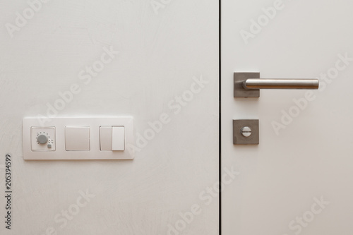 Light switch next to the white door with metallic handle