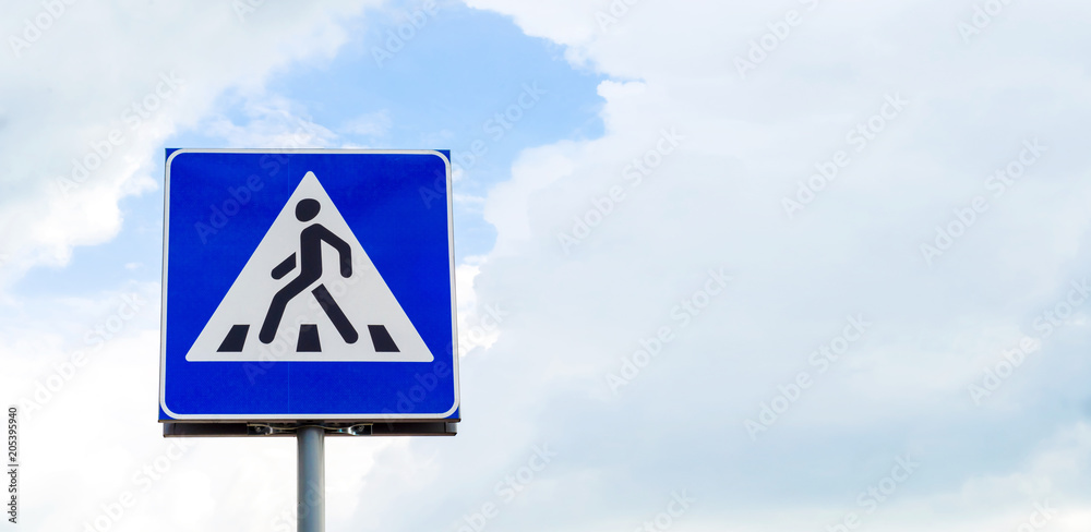 Road sign crossing for a pedestrian on a sky background with clouds Road sign crossing for a pedestrian on a sky background with clouds