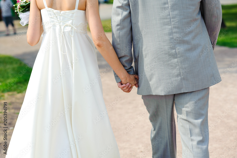 The bride and groom hold hands during the walking in the park. Wedding day in summer.