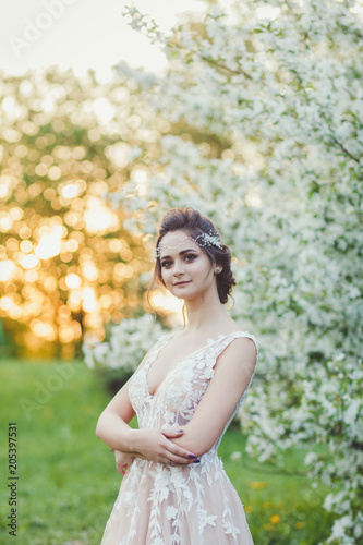 Young beautiful brunette woman in blooming garden. Bride in wedding dress
