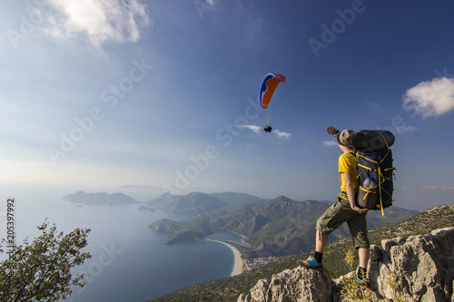 tourist standing on a cliff in mountains with paraglider in air photo
