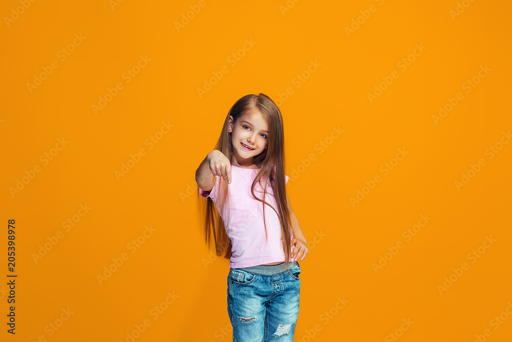 The happy teen girl pointing to you, half length closeup portrait on orange background. The happy teen girl pointing to you, half length closeup portrait on orange background.