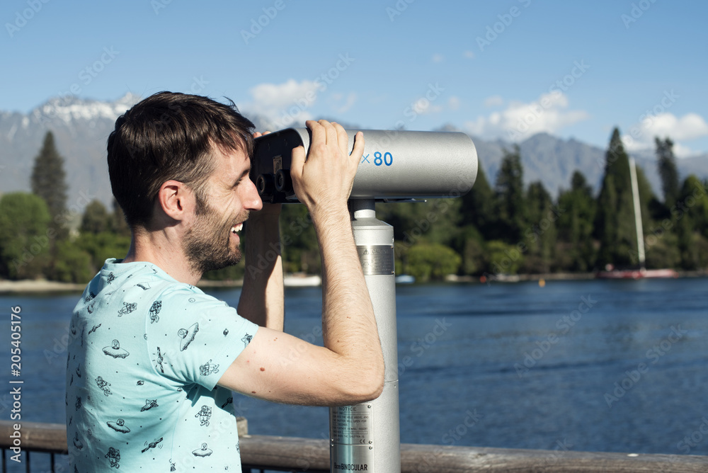 Young men looking through some binoculars near a lake with some mountains and trees