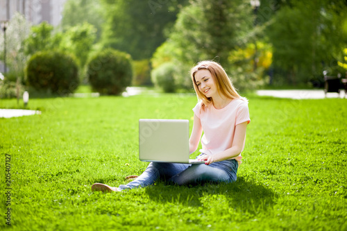 Girl with laptop sitting on the grass and smiling