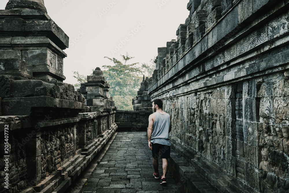 Handsome young tourist feeling the peace of the great Borobudur temple, historical famous place in the java island Indonesia. Lifestyle and travel photography.