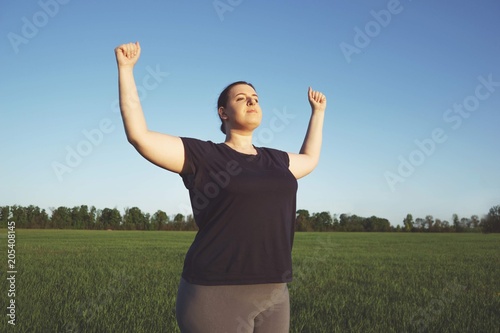 Body positive, freedom, high self esteem, confidence, happiness, success, inspiration. Overweight woman celebrating rising hands to the sky on summer meadow.