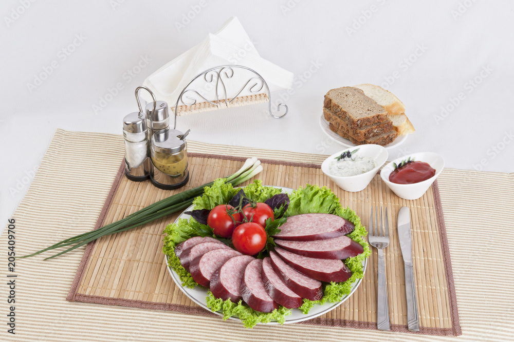 Smoked sausage with tomatoes and lettuce leaves on a plate.
