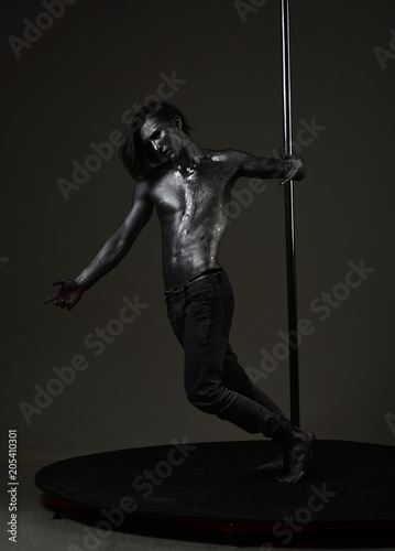 Man with nude torso covered with silver paint, dark background.