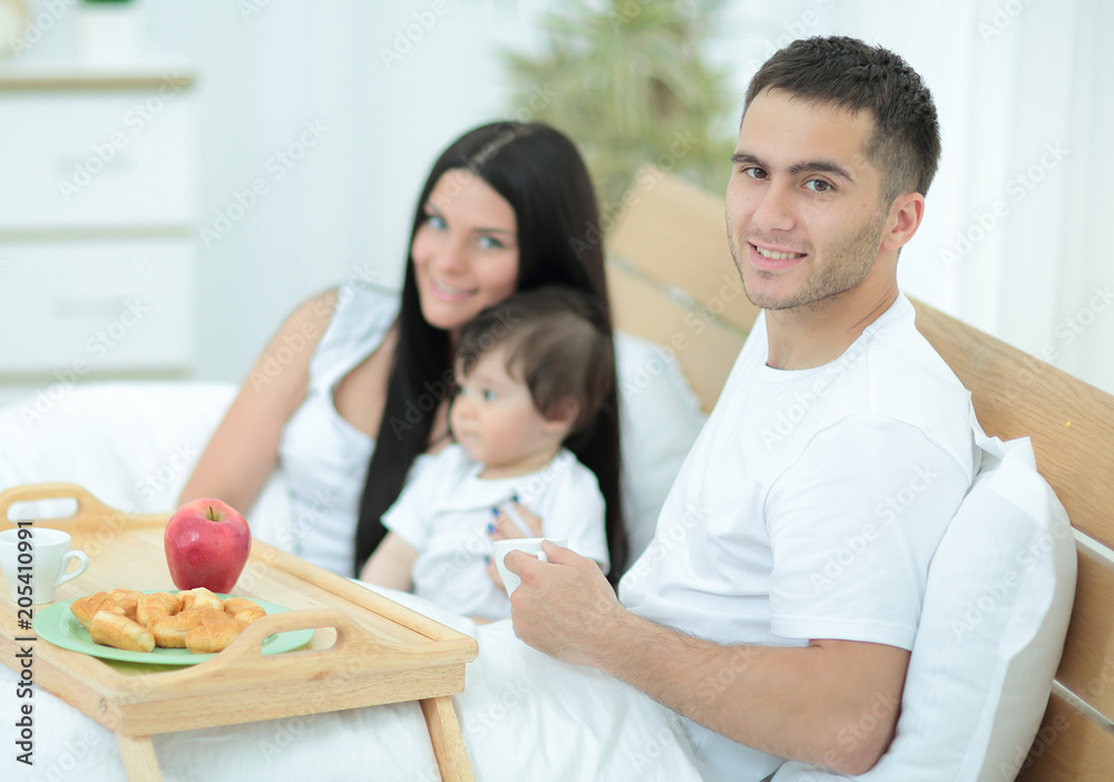 Family with little baby having breakfast in the bed.