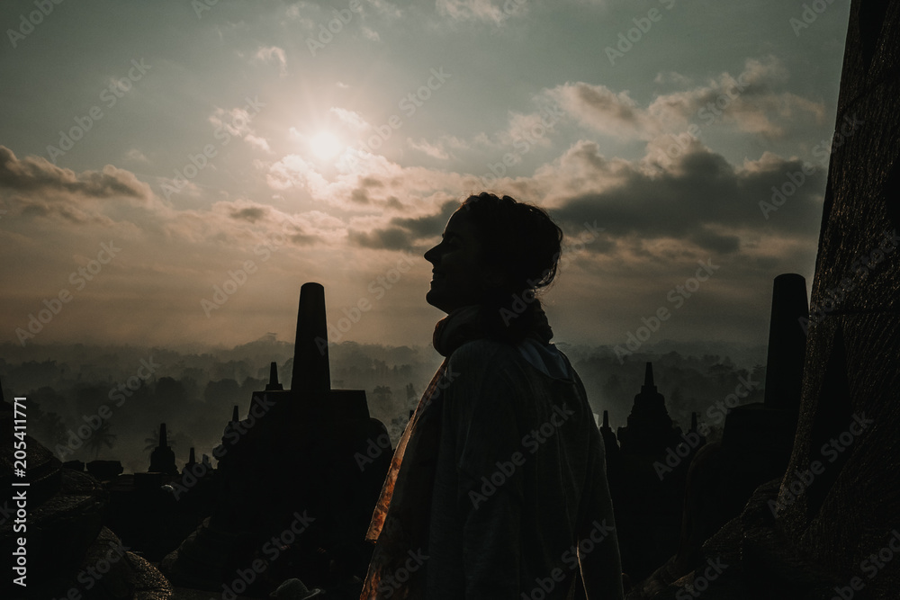 Silhouette of a tourist feeling the peace and spirituality of the great Borobudur temple, historical famous place in the java island Indonesia. Lifestyle and travel photography.