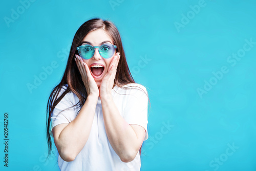 Pretty caucasian brunette girl wears sunglasses have happy surprised face expression on blue background