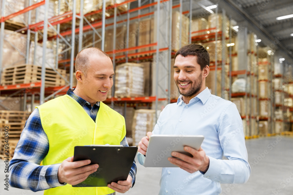 wholesale, logistic business and people concept - warehouse worker and businessman with clipboard and tablet pc computer