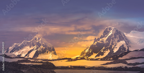 The wonderful fairy tale mountain landscape. The snow-covered Antarctic mountain crests on the sunrise sunset colorful background. Stunning panoramic view. Spectacular golden blue color combination.