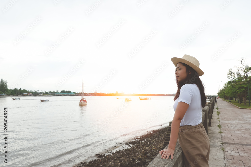 Side view of happy asian woman in hat standing and looking at river in evening sunset. Side view of happy asian woman in hat standing and looking at river in evening sunset.