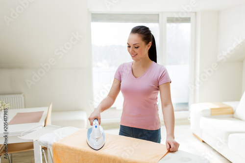 housework and household concept - happy woman or housewife ironing bath towel on iron board at home