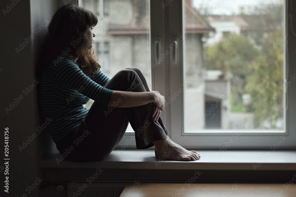 © Tunatura - Sad young woman sitting on the window, watching out