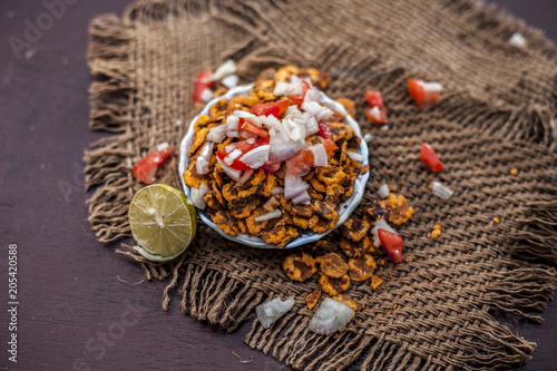 Popular Indian & Asian snack or junk food chana chur garam in a clay bowl on wooden surface with onions,lemon and tomatoes. photo