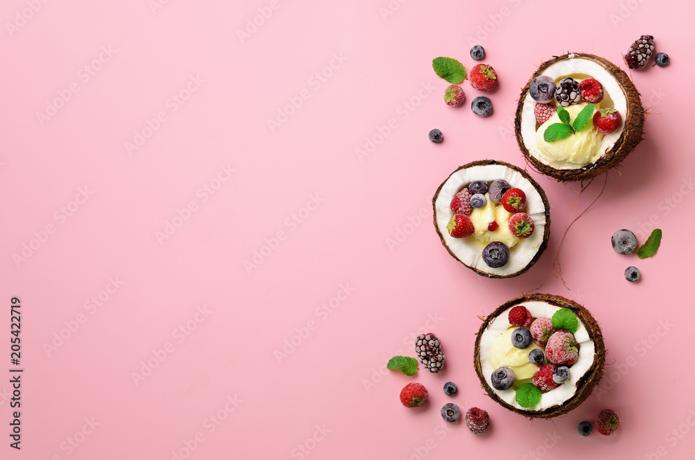 Coconut ice cream with fresh berries in coconuts halves on pink background with copy space. Top View. Pop art design, creative summer concept. Food in minimal flat lay style.