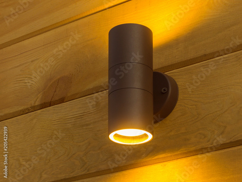 Outdoor exterior small cylinder lamp on wooden wall. External illumination