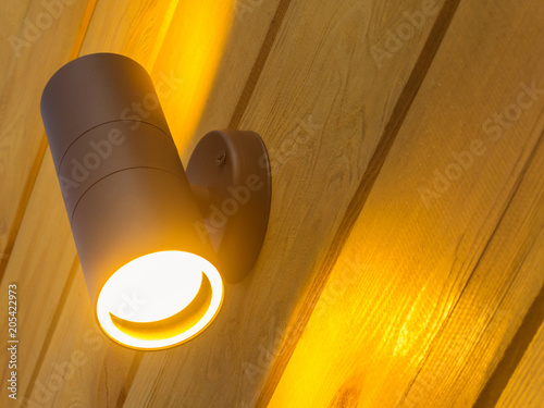 Outdoor exterior small cylinder lamp on wooden wall. External illumination