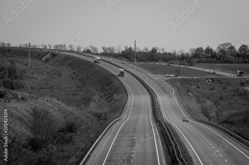 A two lane hilly highway black and white with cars far away