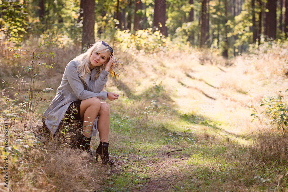 A young, blonde woman walking through the forest on a sunny autumn day. A young, blonde woman walking through the forest on a sunny autumn day.